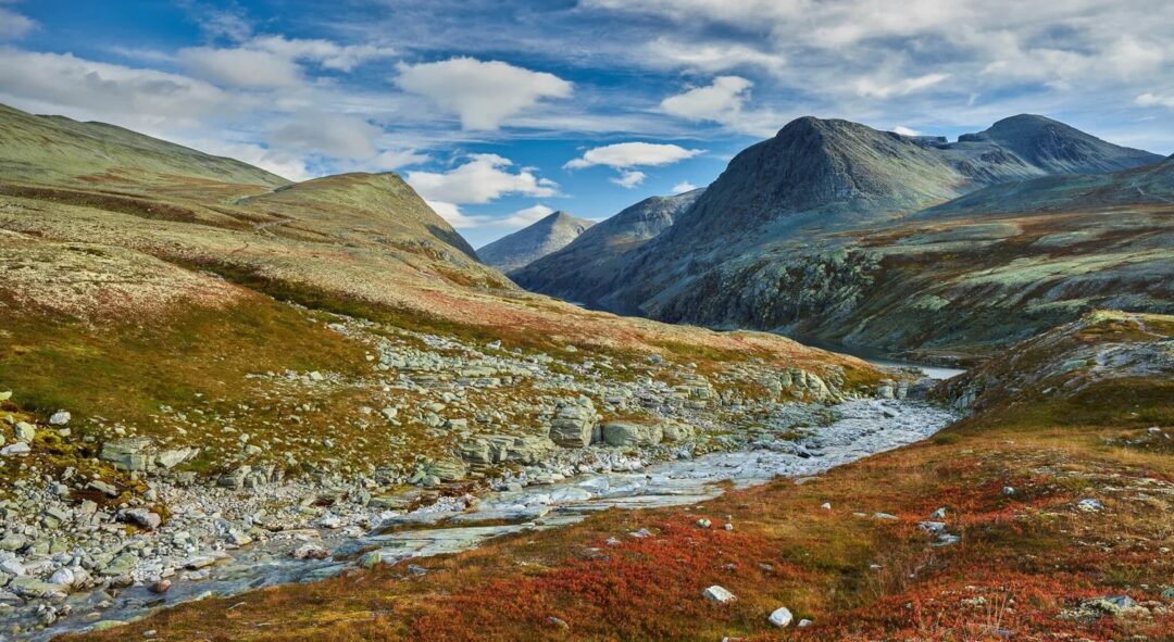 Norwegian mountain valley with a winding river through tundra hills under a cloudy sky