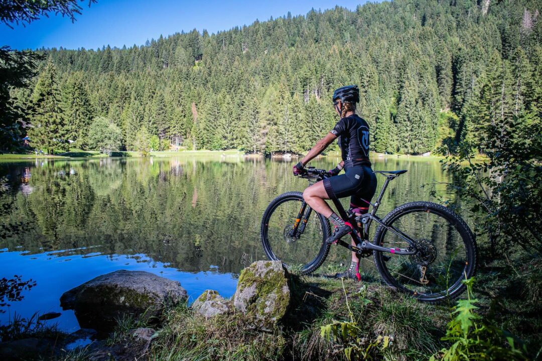 Woman mountain biking by a forest lake in the mountains.