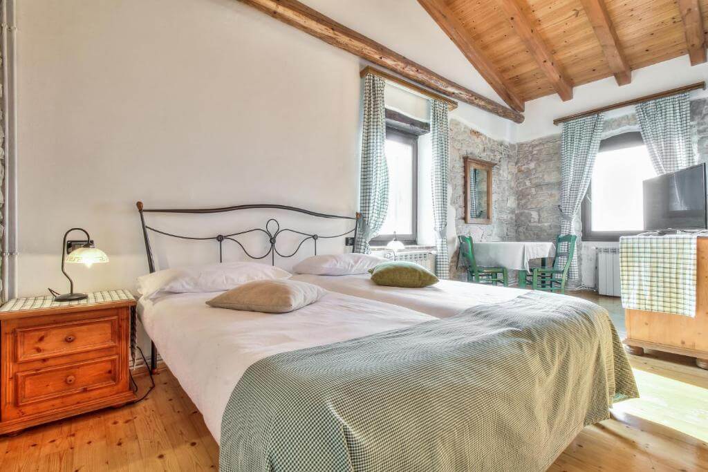 Rustic bedroom interior with double bed, wooden ceiling beams, stone wall and windows with curtains