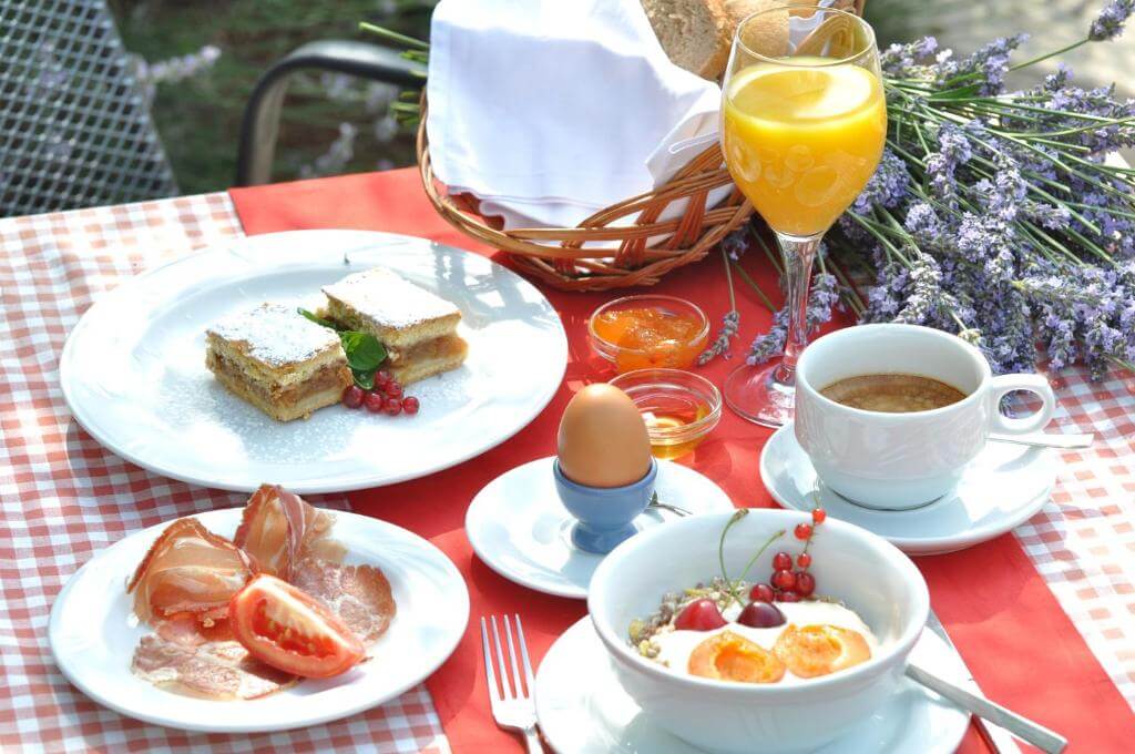 Breakfast table with pastries, eggs, juice and coffee, decorated with lavender on a red check cloth