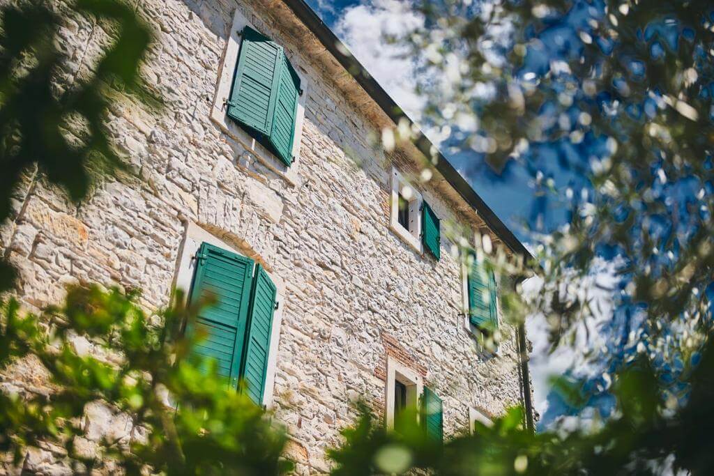 Stone houses with green shutters surrounded by trees in a sunny Mediterranean setting
