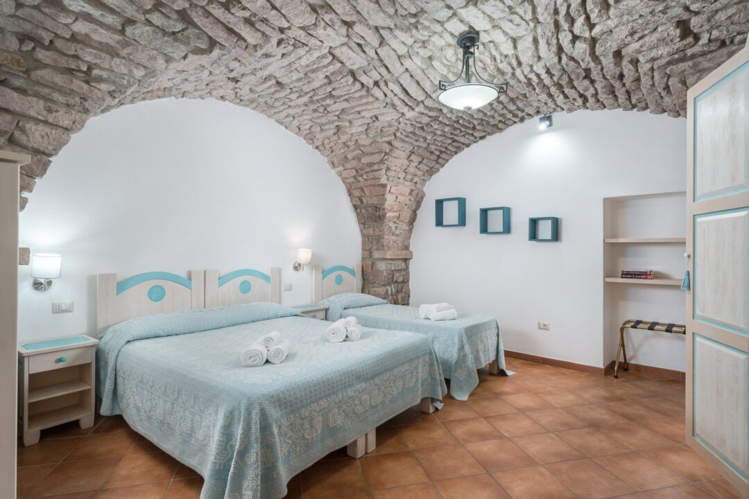 Stone-arched bedroom interior with a double bed, tiled floor, and bedside cabinets in a bright suite