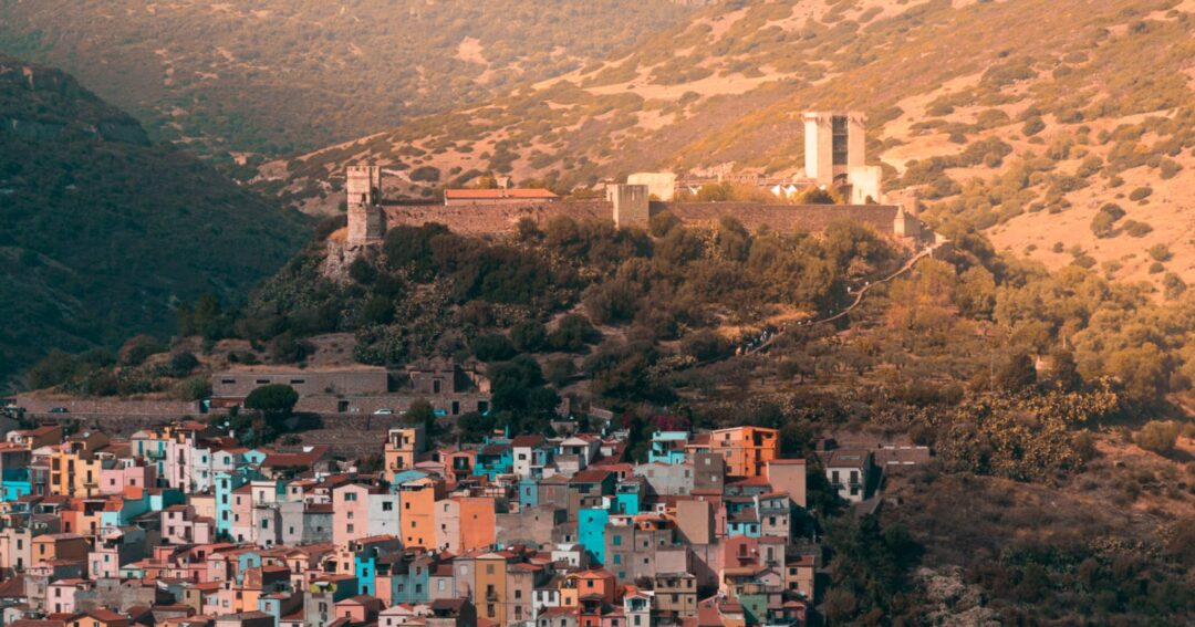 Hilltop village in Sardinia with pastel houses and distant church/monastery at sunset over mountains