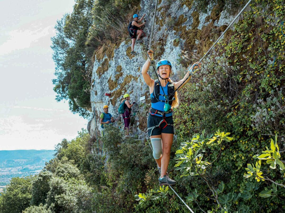 Women adventure hiking on a rope-assisted cliff path, wearing harnesses and helmets in coastal terrain