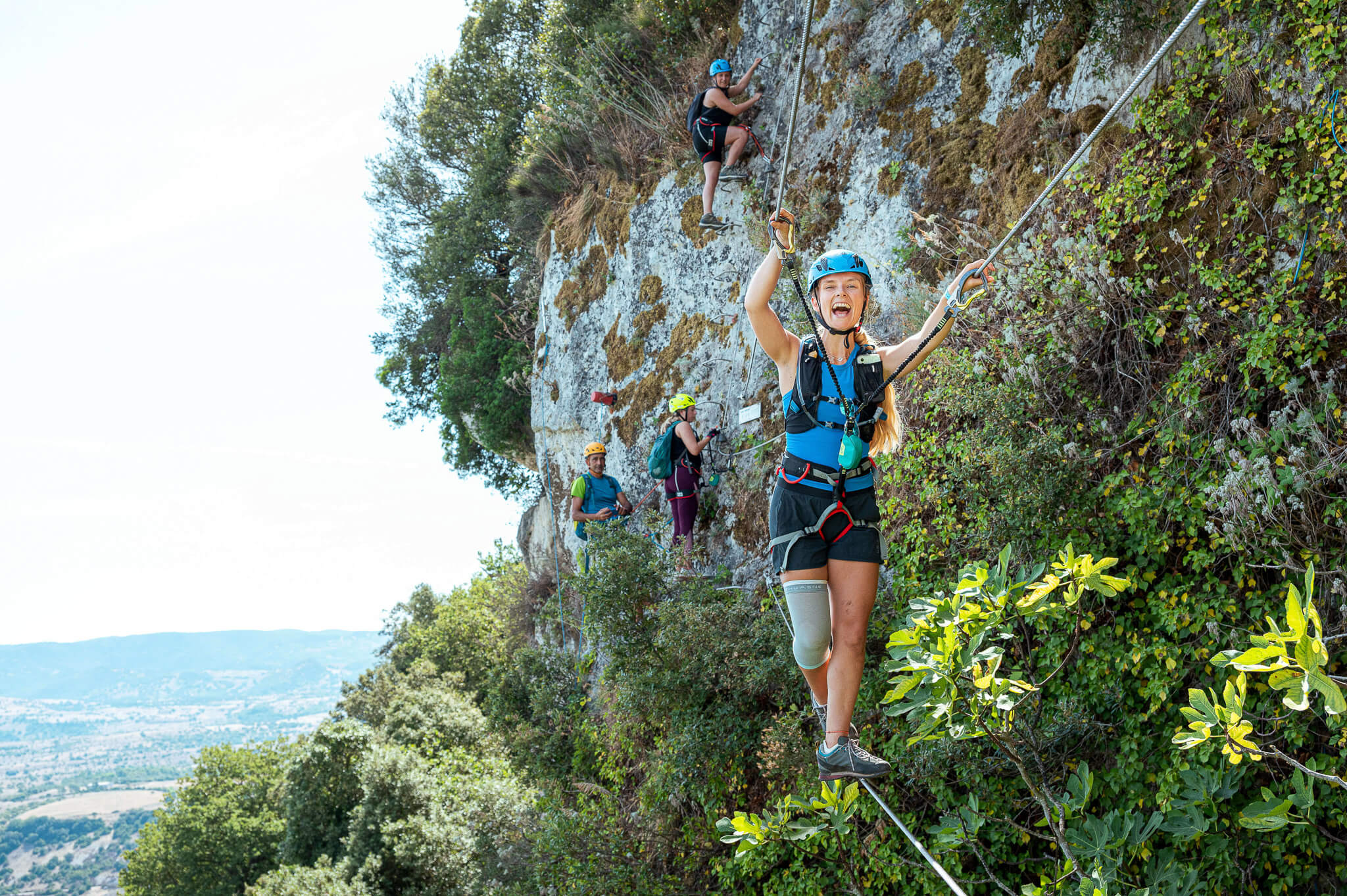 Women rock climbing on a rope-guided cliff face, wearing harnesses and helmets outdoors