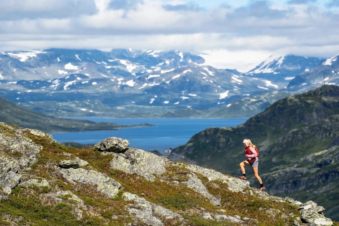 Woman hiking on a rocky ridge with fjord and snowy peaks in Jotunheimen, Norway