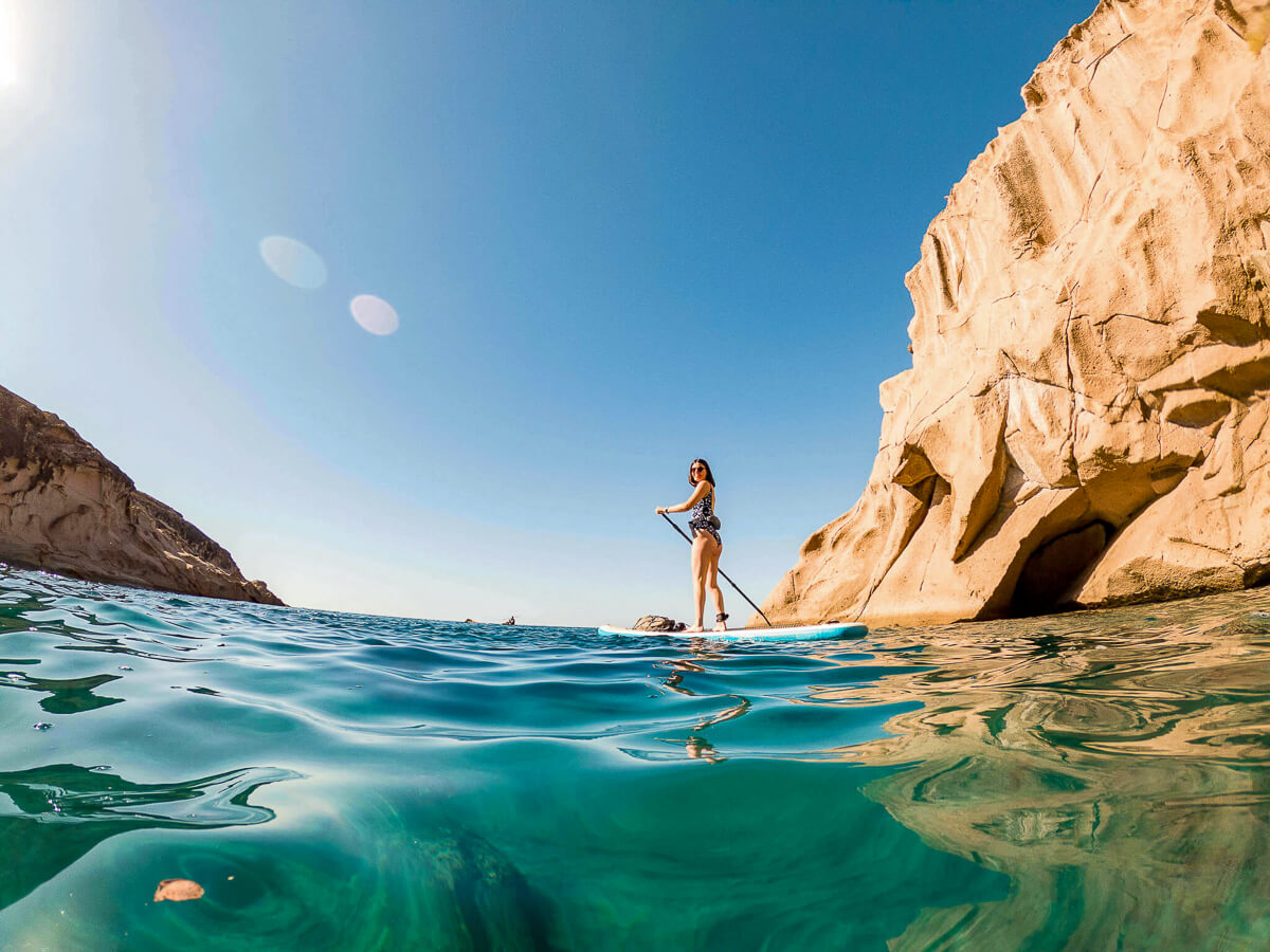 Woman on a stand-up paddleboard in clear sea near rocky coastal cliffs