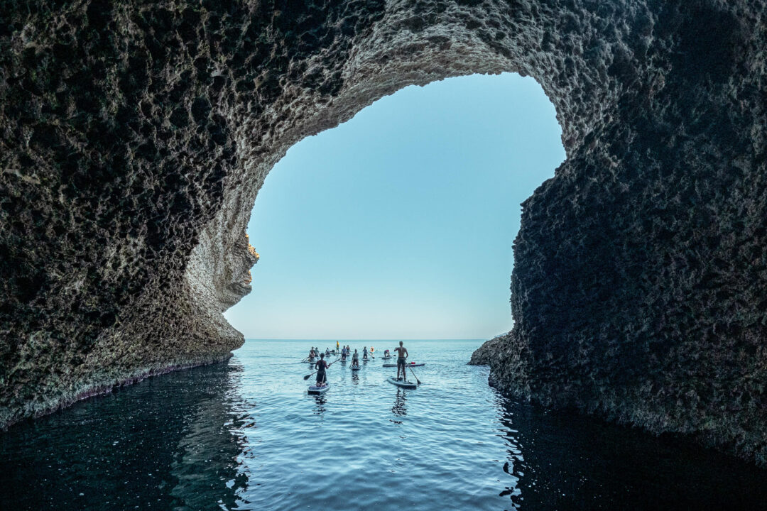 Women on stand-up paddleboards in a sea cave, Sardinia