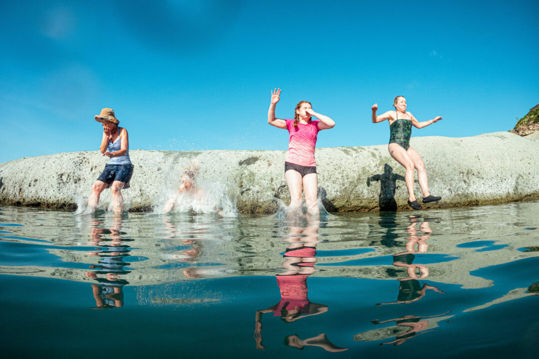 Women SUP paddleboarding on calm sea, jumping off their boards against a blue sky