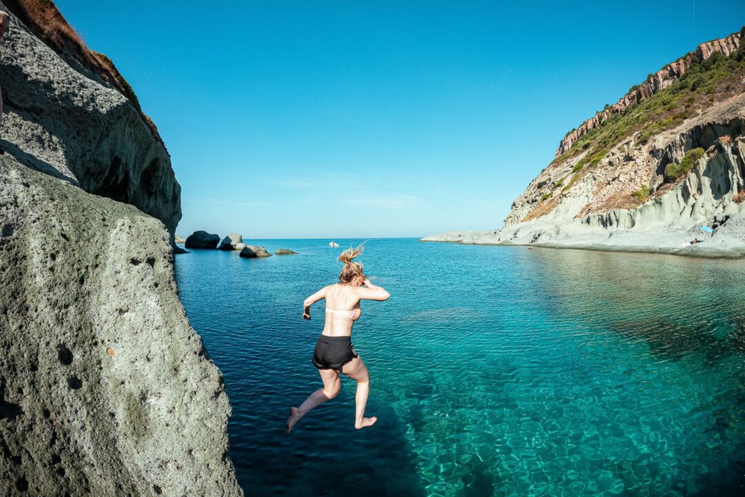 Woman SUP paddleboarding in clear turquoise water beside rocky cliffs and coves