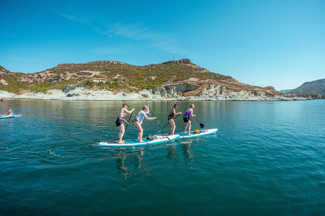 Women paddleboarding (SUP) on calm sea with Sardinian coastline and hills in the background
