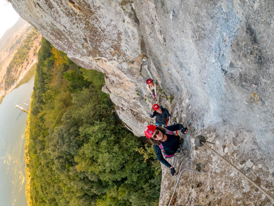 Women rock climbing on a cliff wall, harnesses on a via ferrata route