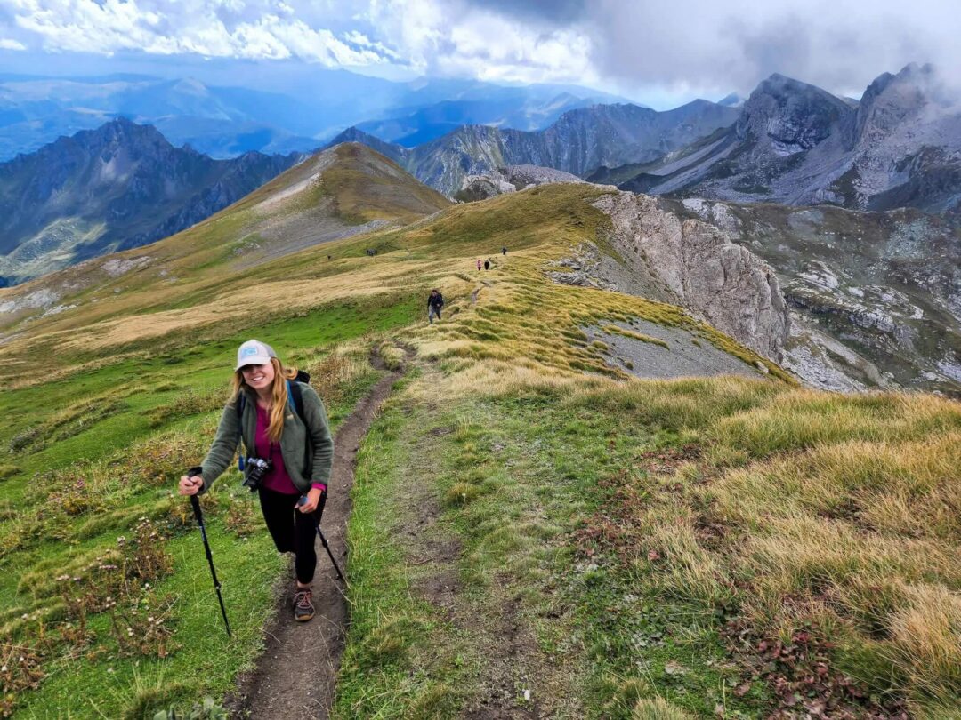 Women hiking along a mountain trail with Alpine peaks and a wide valley view