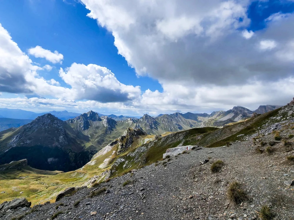 Mountain ridgeline and valley view under dramatic clouds, with winding trails in the distance