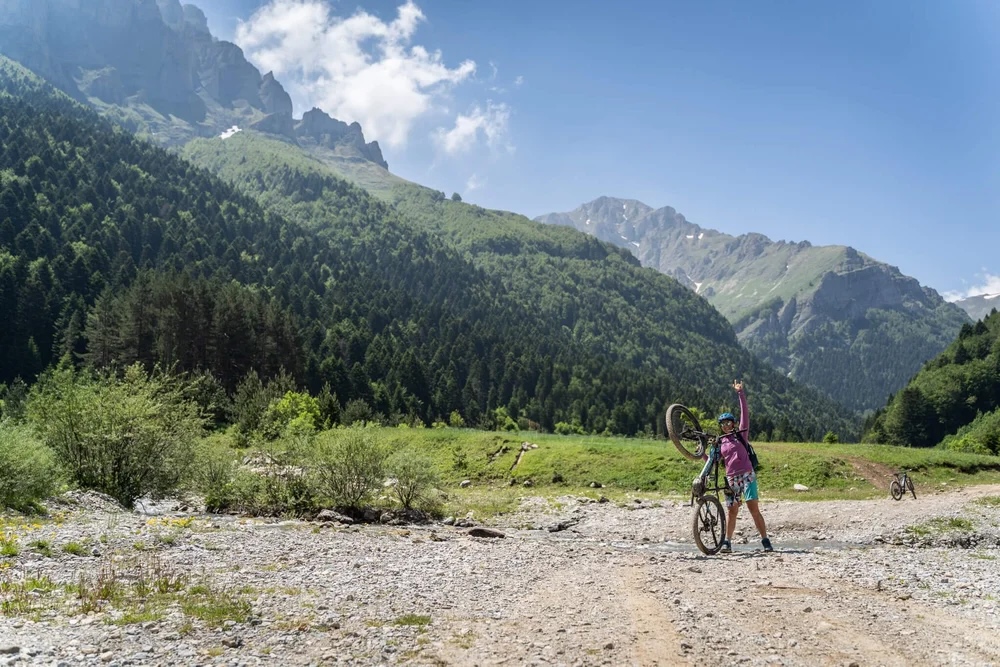 Woman with an e-bike on a mountain trail through a green valley landscape
