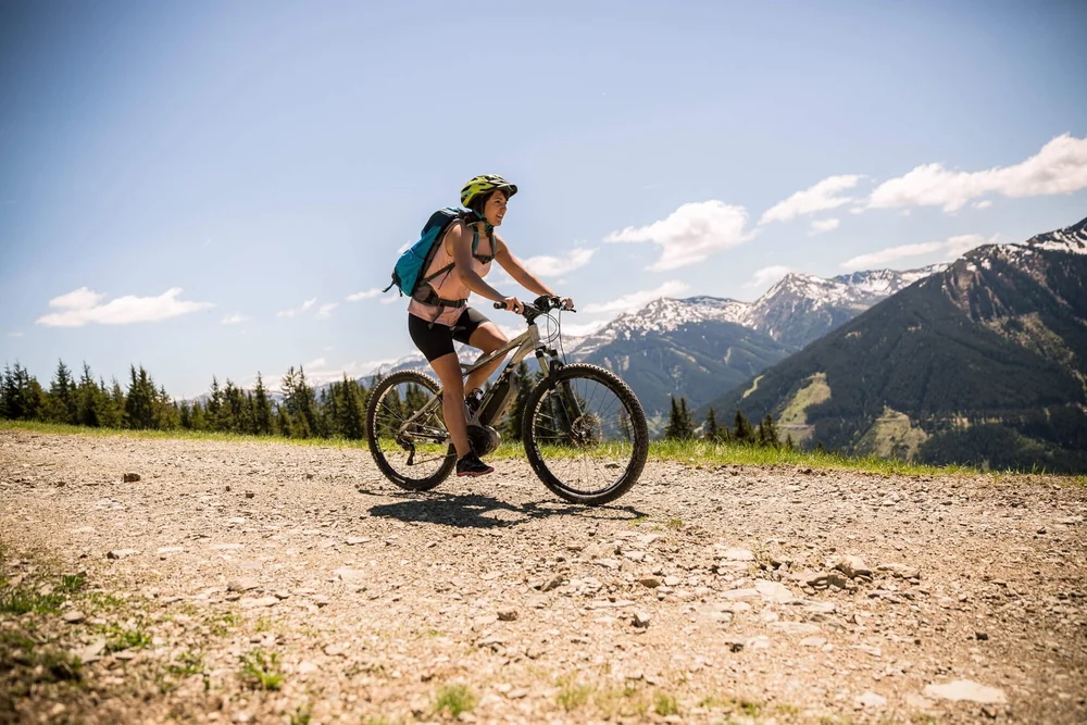 Woman mountain biking on a gravel track with snowy mountains in the background