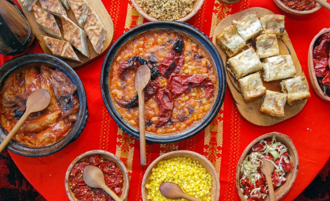 Bowls of hearty stew with bread pieces and side dips on a red tablecloth, assorted appetisers.