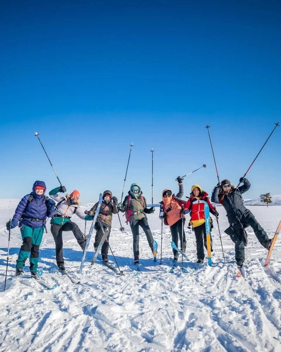 Women skiing on a snowy field with ski poles under a clear blue sky during a winter expedition
