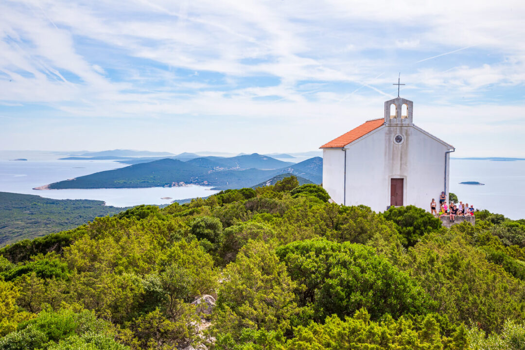 Woman group walking near a white chapel on a lush island hillside overlooking calm waters