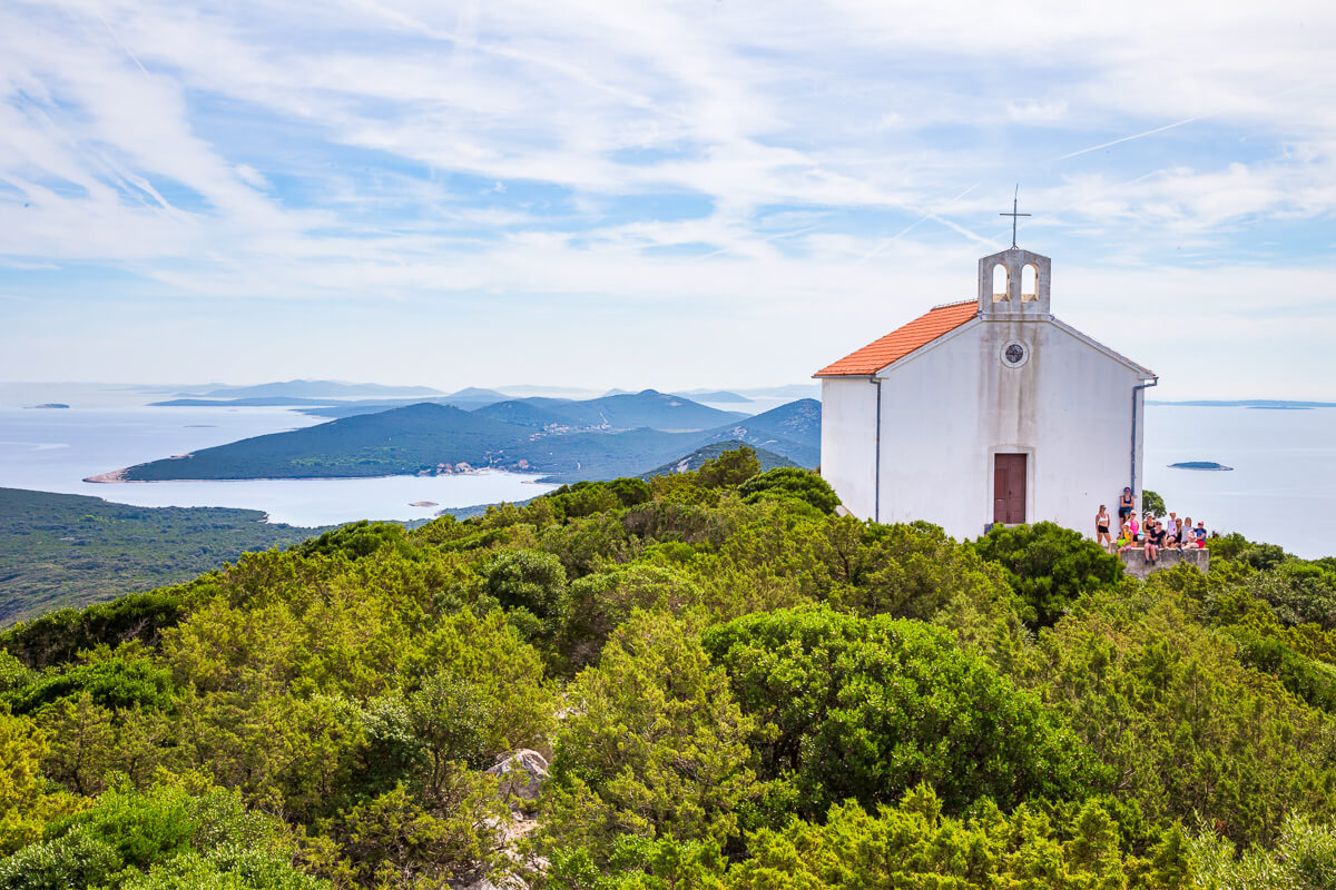 Woman group walking near a white chapel on a lush island hillside overlooking calm waters