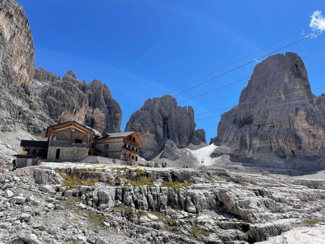 Via ferrata hut in the Dolomites with rocky peaks and snowy valley under a clear blue sky