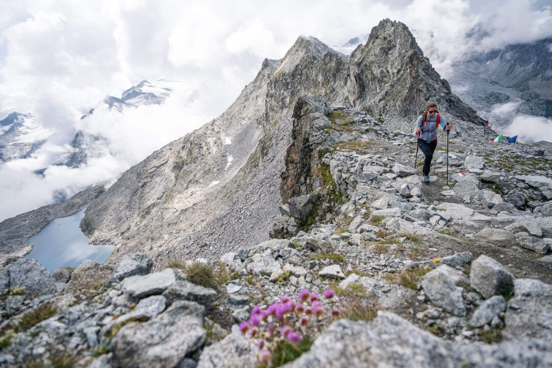 Woman hiking along a rocky mountain ridge with dramatic Alpine peaks and clouds