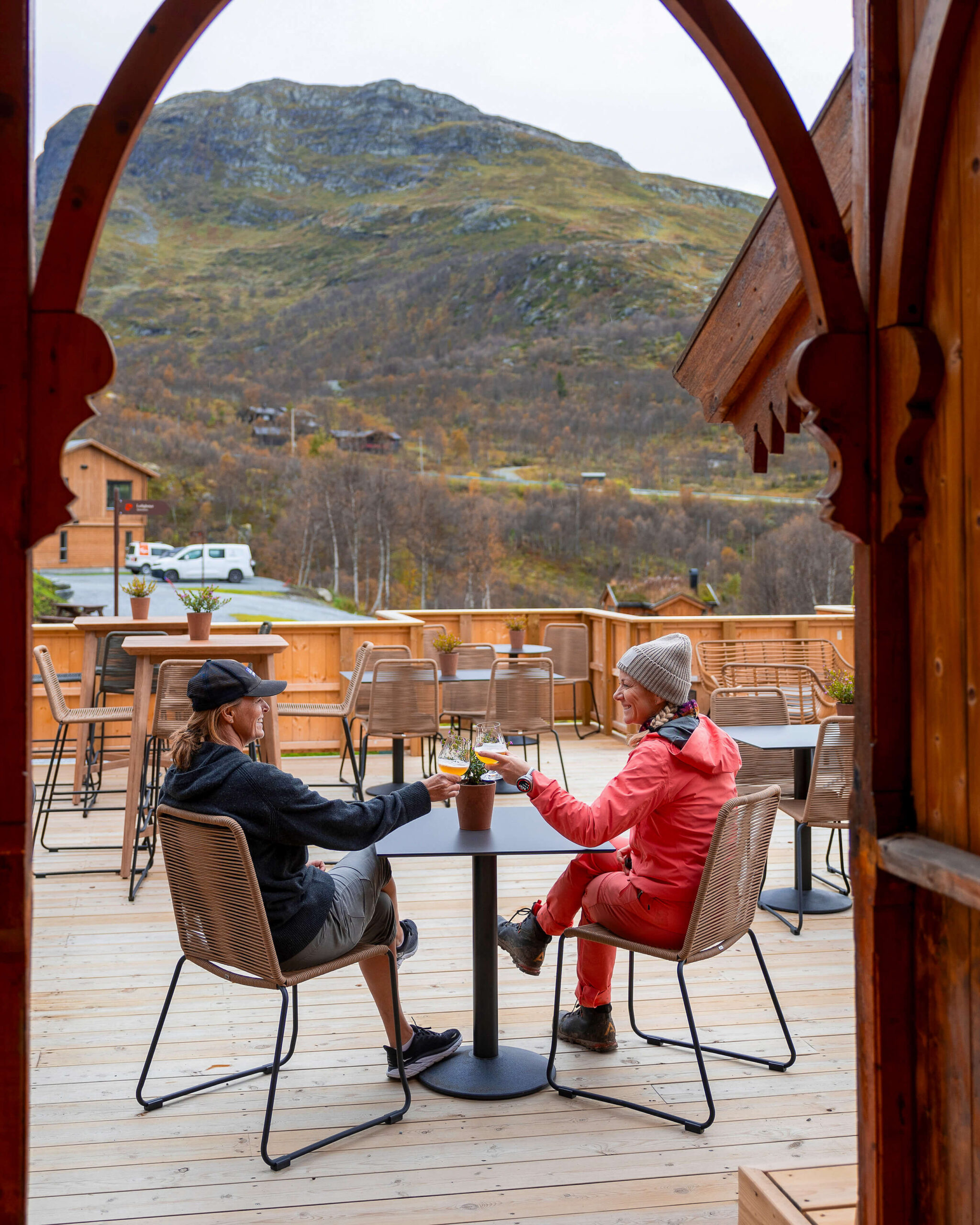 Two women on a wooden terrace in Norway, enjoying drinks with mountain views