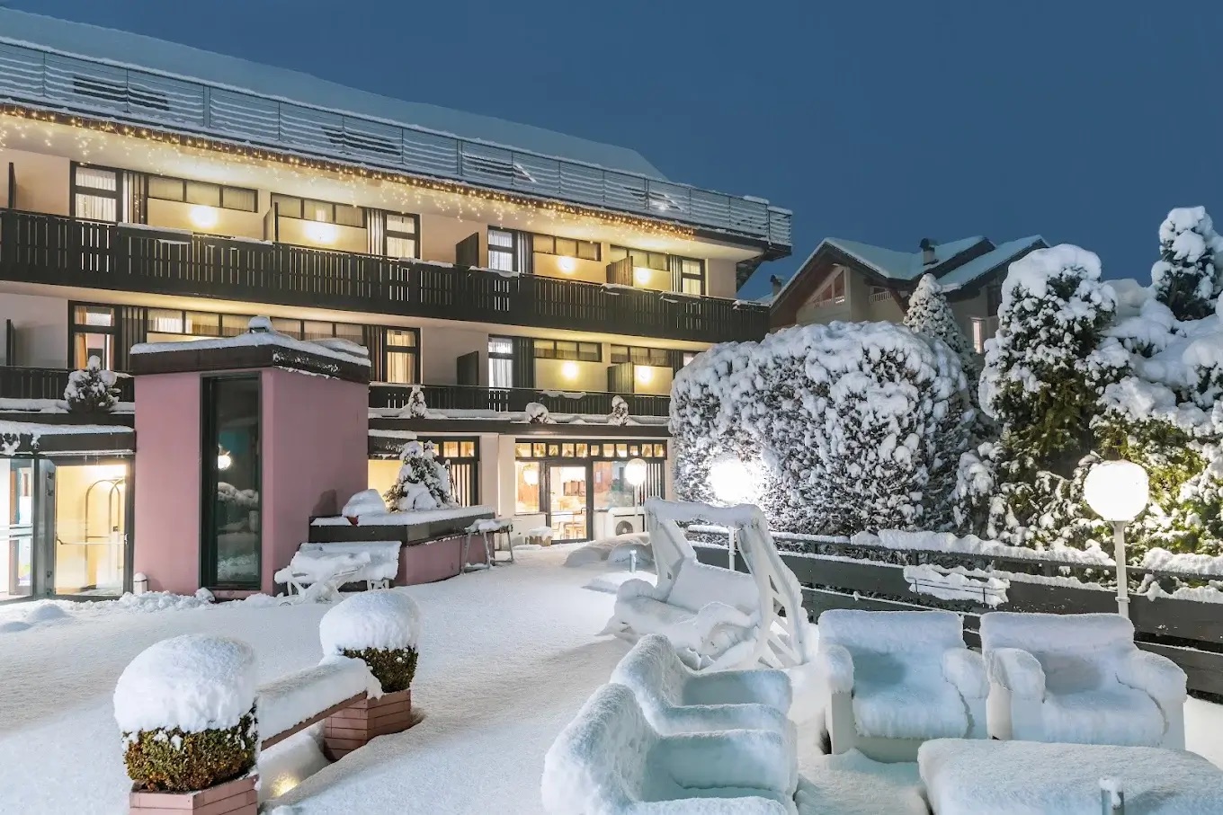 Snow-covered mountain hotel exterior with warm lights and winter garden, suitable for snowshoeing holidays