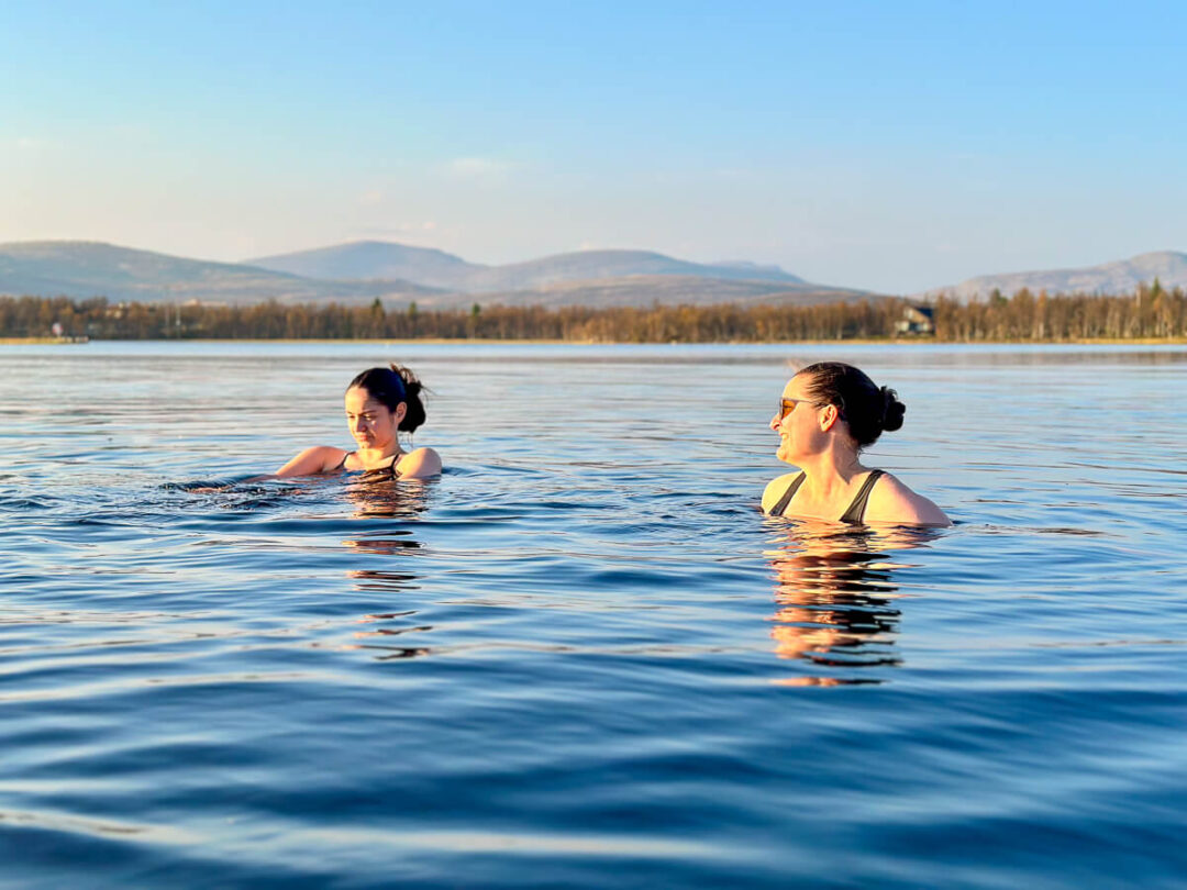 Women swimming in a calm lake in Norway at a lakeside yoga holiday, clear blue water and mountains in view