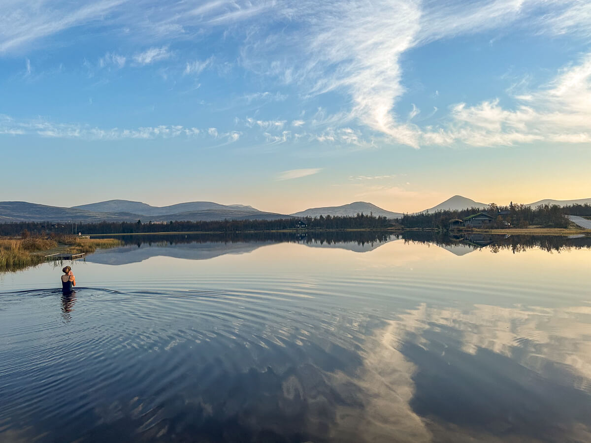 Woman wading in a calm lake at sunrise, with mountains in Norway