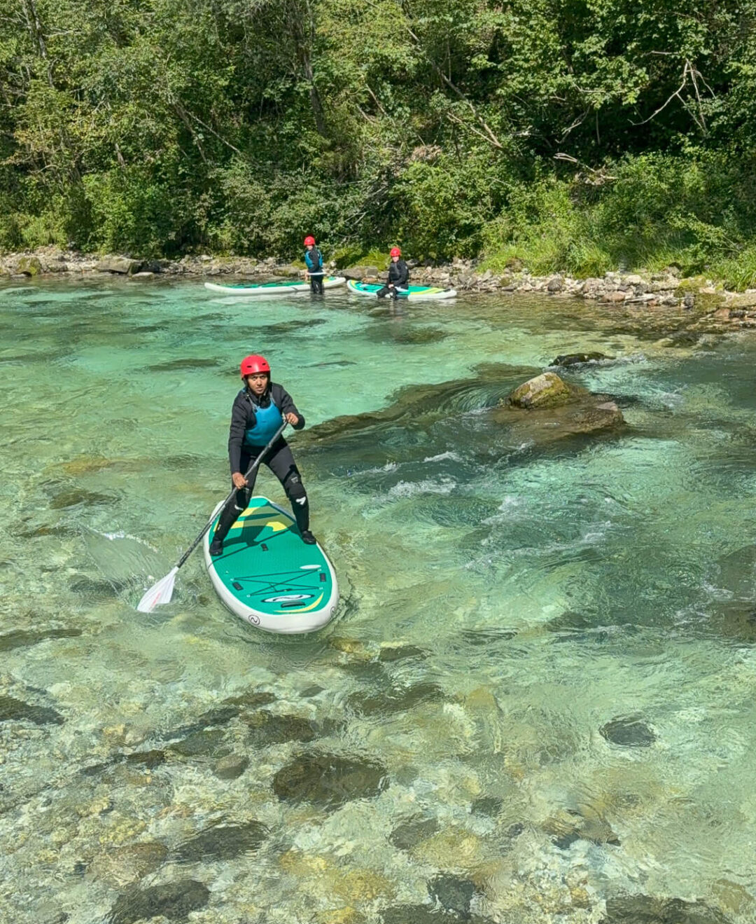 Women stand-up paddleboarding on a clear, fast-flowing river with rocks and greenery in the background