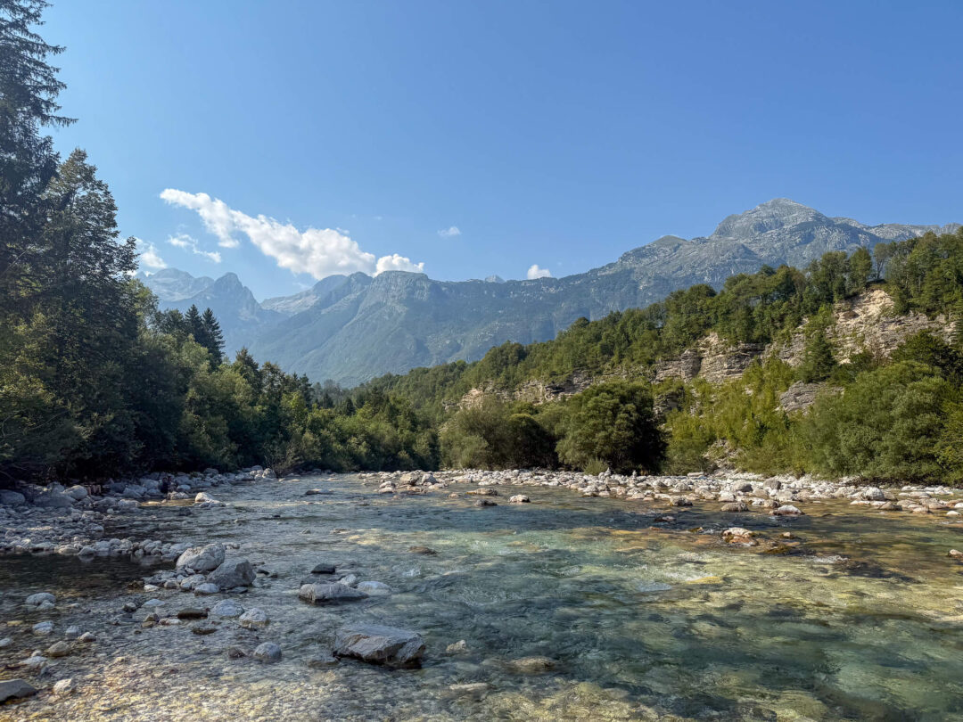 Clear river rapids in Slovenia with forested banks and mountain peaks under blue sky