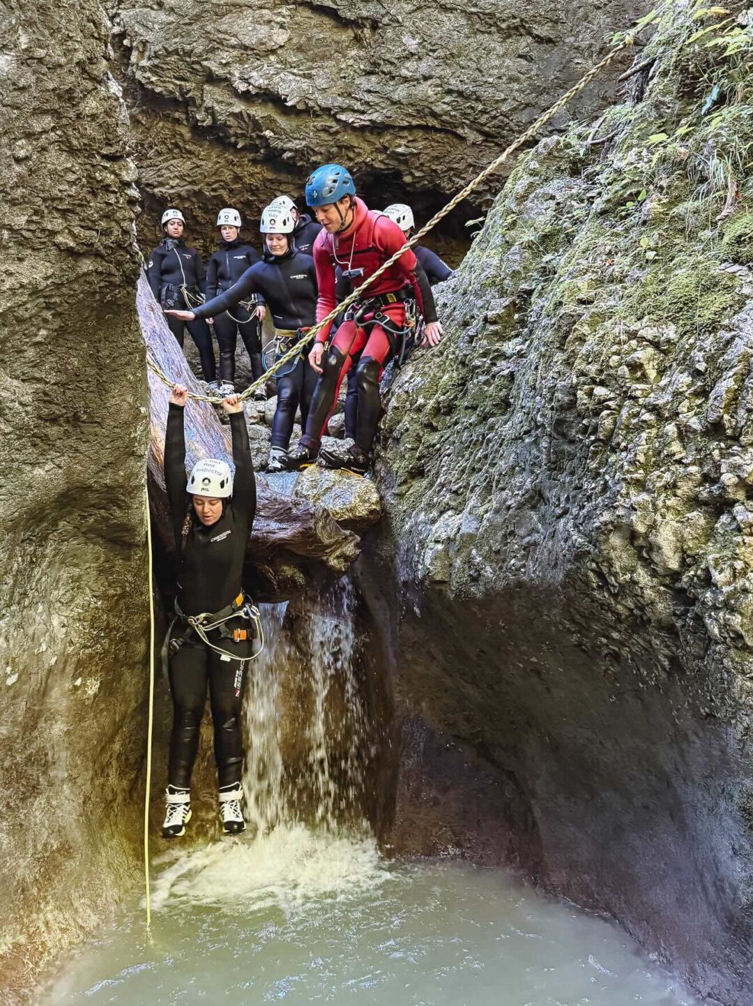 Women canyoning in a rocky gorge, wearing helmets, wetsuits and ropes in flowing water