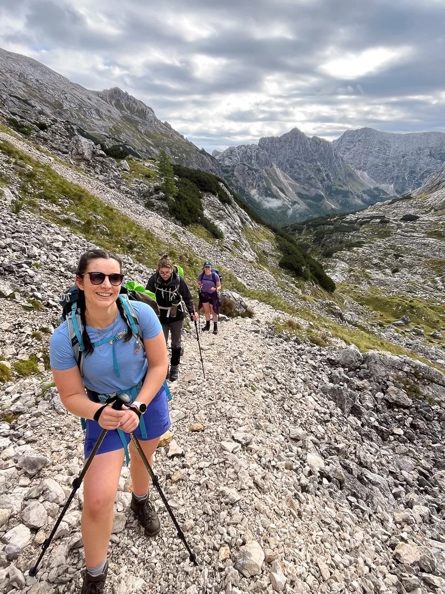 Women hiking on a rocky alpine trail through the mountains under a cloudy sky
