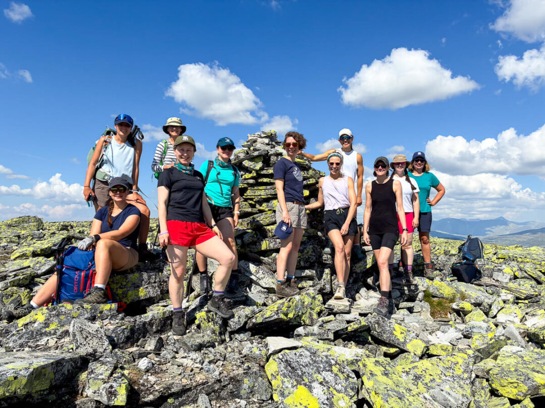 Women hiking on a rocky mountain summit under a blue sky with expansive valley views