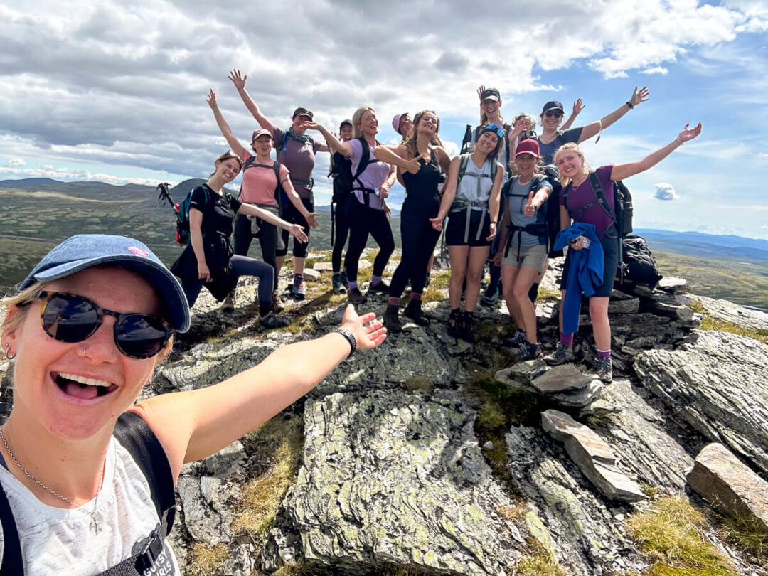 Women hiking on a mountain ridge in Norway, smiling with arms out against a valley view.