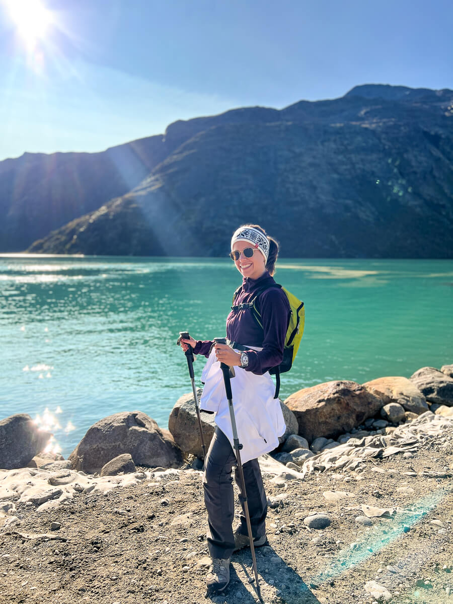 Woman hiking by a turquoise fjord with trekking poles, mountains in bright daylight