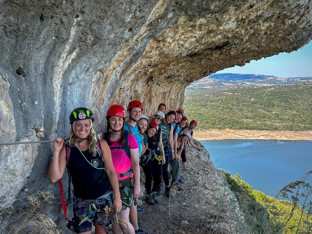 Women hiking along a rocky sea cliff in Sardinia, group posing overlooking turquoise water