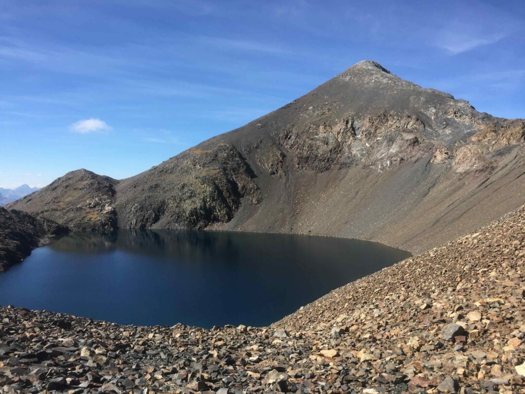 High-altitude mountain lake with rocky shore beneath steep mountain peaks
