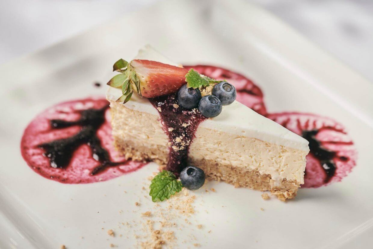 Cheesecake slice topped with blueberries, herbs and a strawberry on a plate