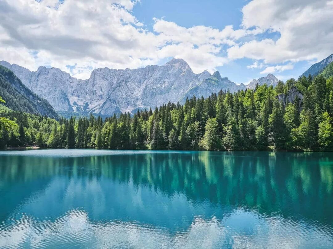 Turquoise mountain lake with pine forest and Alpine peaks under a blue sky in Europe