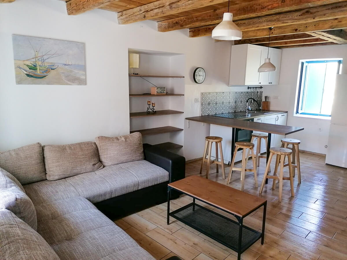 Wood-beamed living room with sofa, coffee table and small kitchen area with bar stools