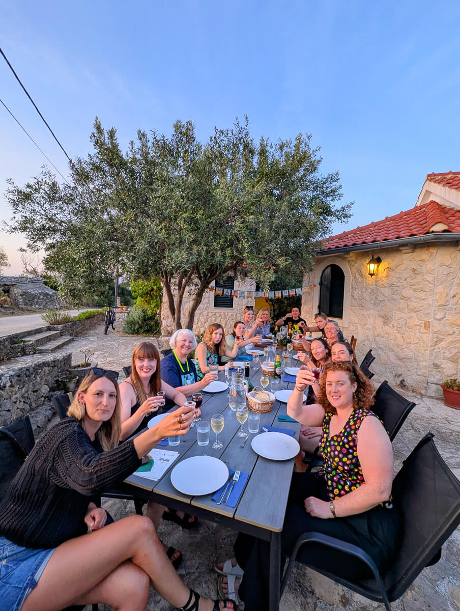 Women dining outdoors at a long table with drinks and food in a Mediterranean courtyard