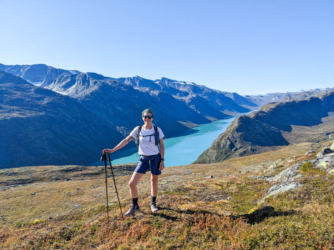 Woman hiking in Norway on a mountain trail with trekking poles, overlooking valley and peaks