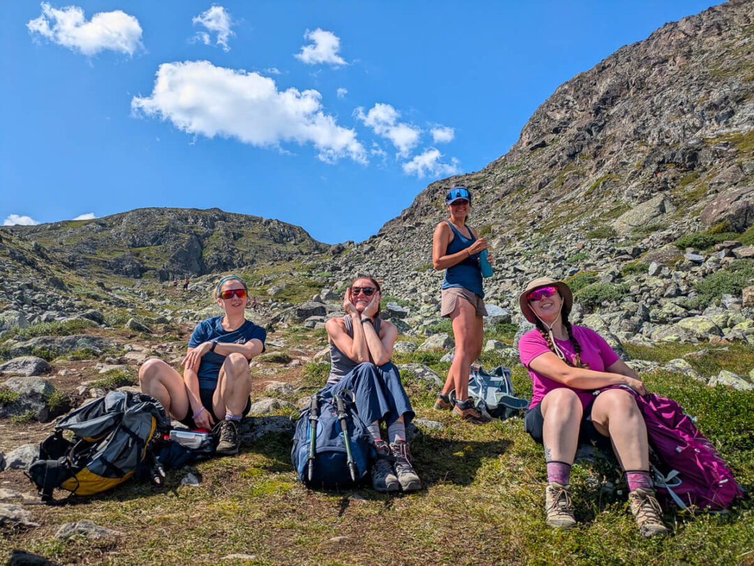 Women on a hiking break with backpacks on a Norwegian mountain trail under a blue sky