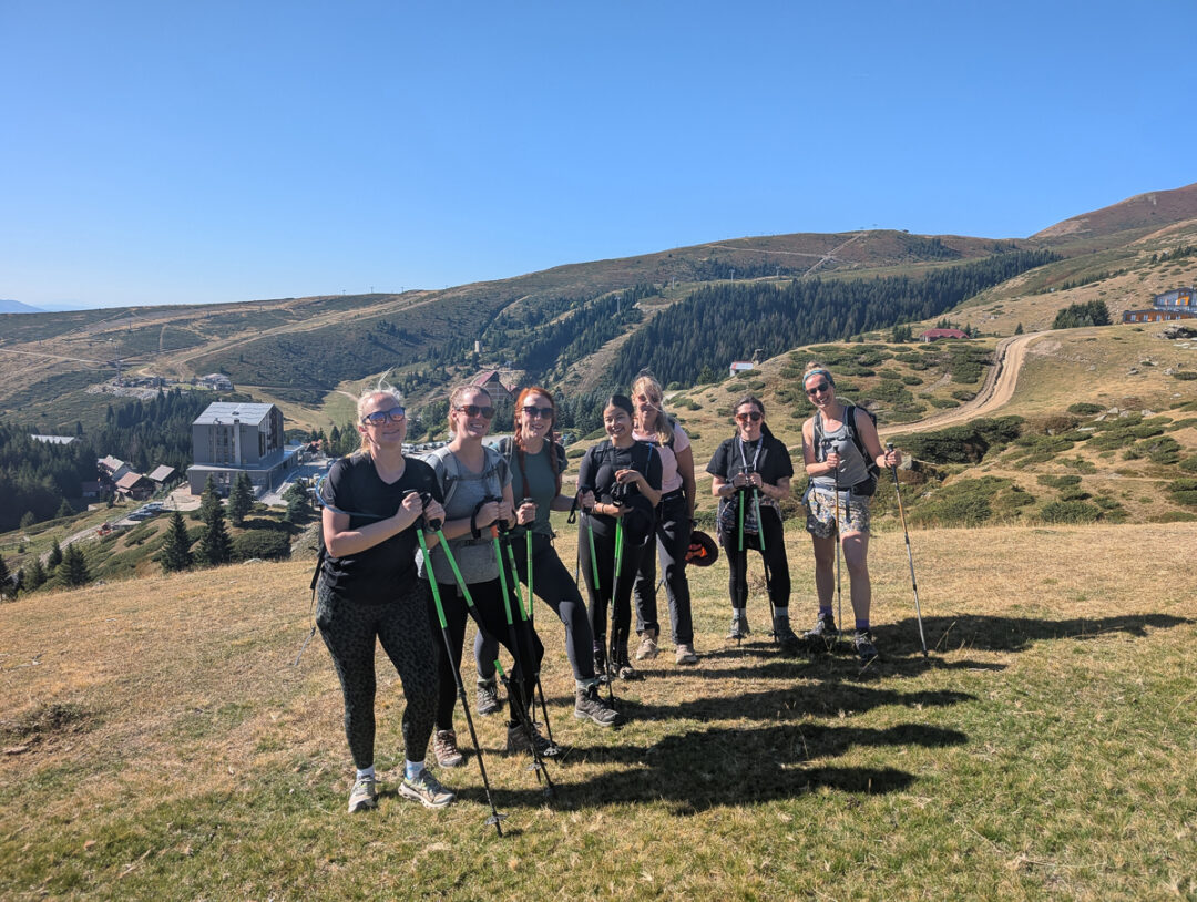 Group of women hikers with trekking poles standing on a mountain trail under a blue sky