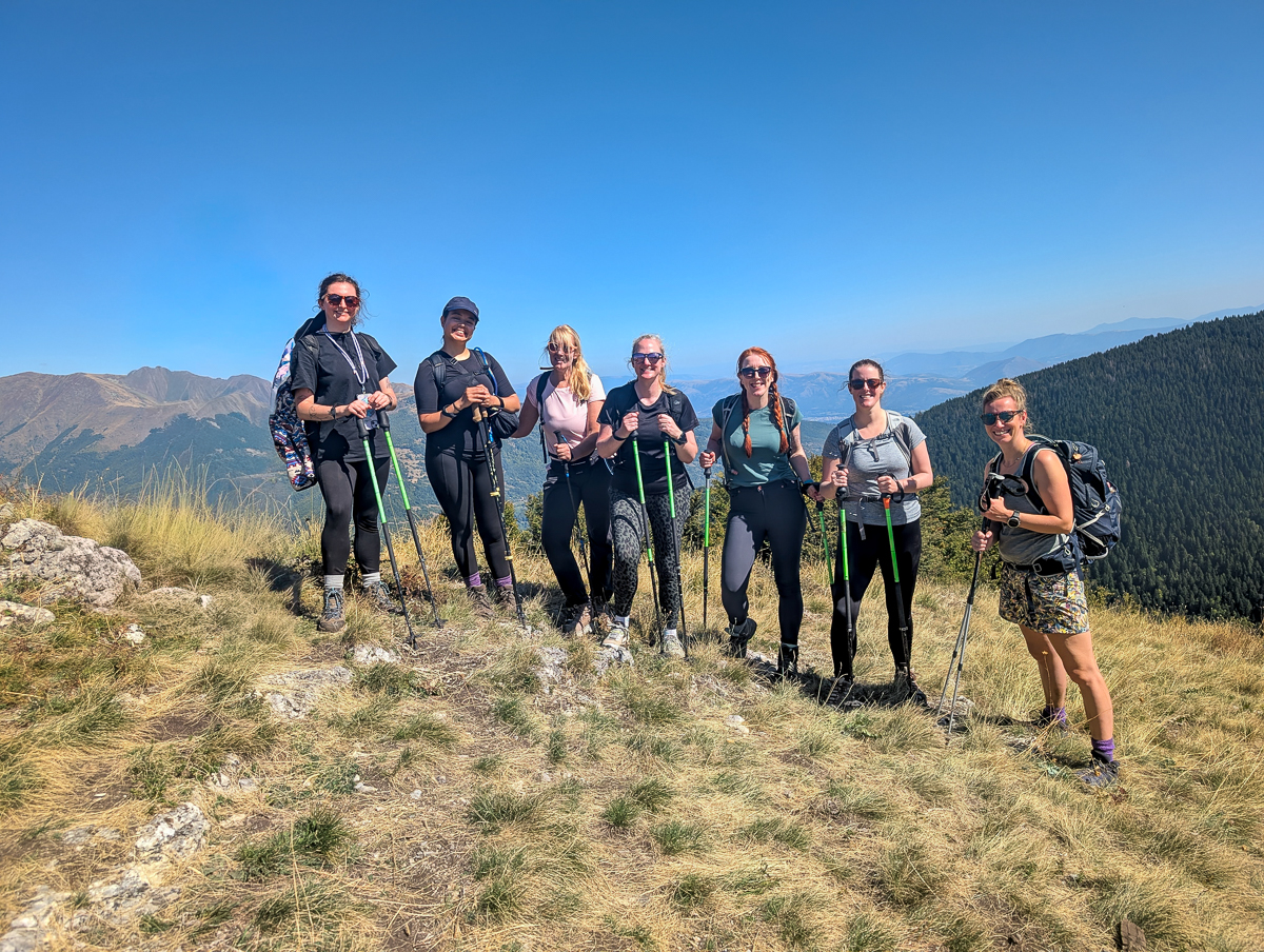Women hikers with trekking poles on a mountainside trail under blue sky
