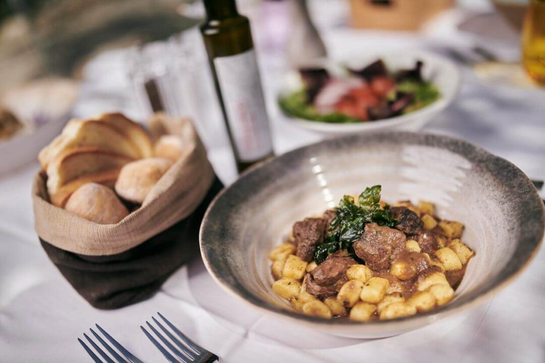 Served dinner plate with meat and potatoes, with bread basket and salad on a restaurant table