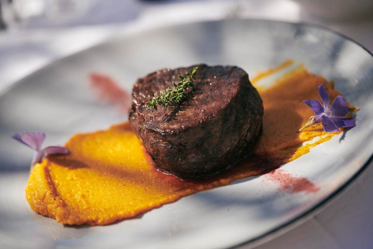 Plated beef steak with polenta and edible flowers on a white dinner dish