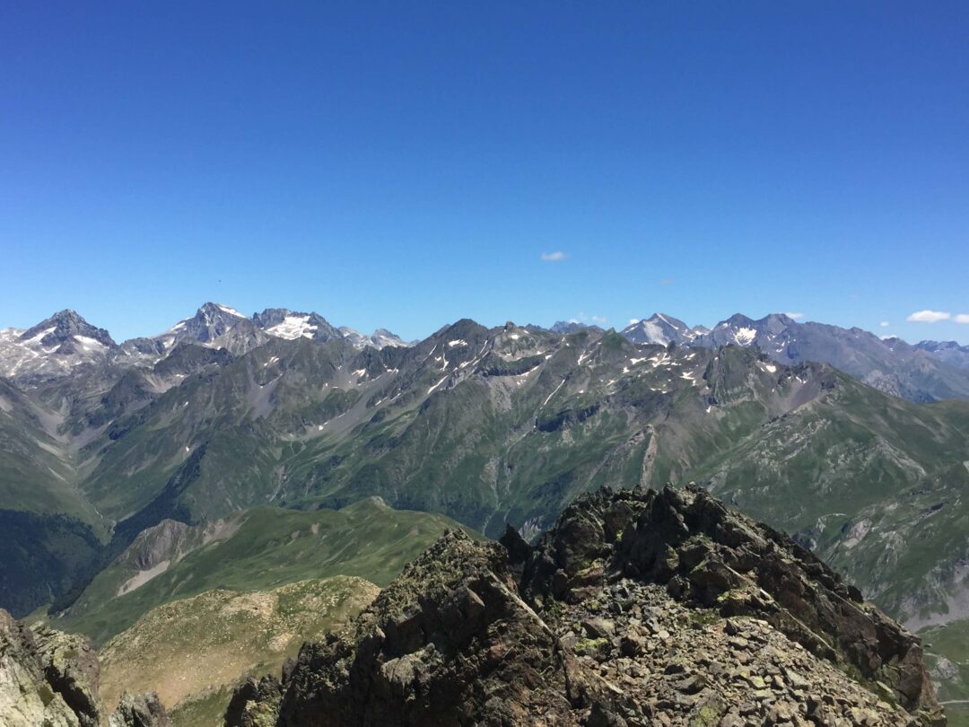 View from a mountain ridge over the Spanish Pyrenees, showing rugged peaks and valleys under a clear blue sky